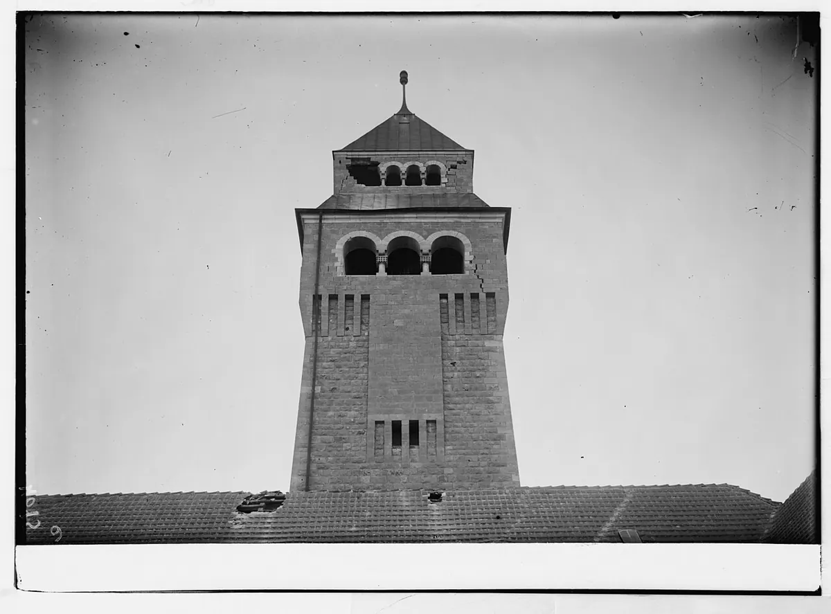 מגדל אבן גבוה ומרובע עם חלונות קשתיים בראשו. בחלק העליון נראים סדקים ואבנים חסרות.