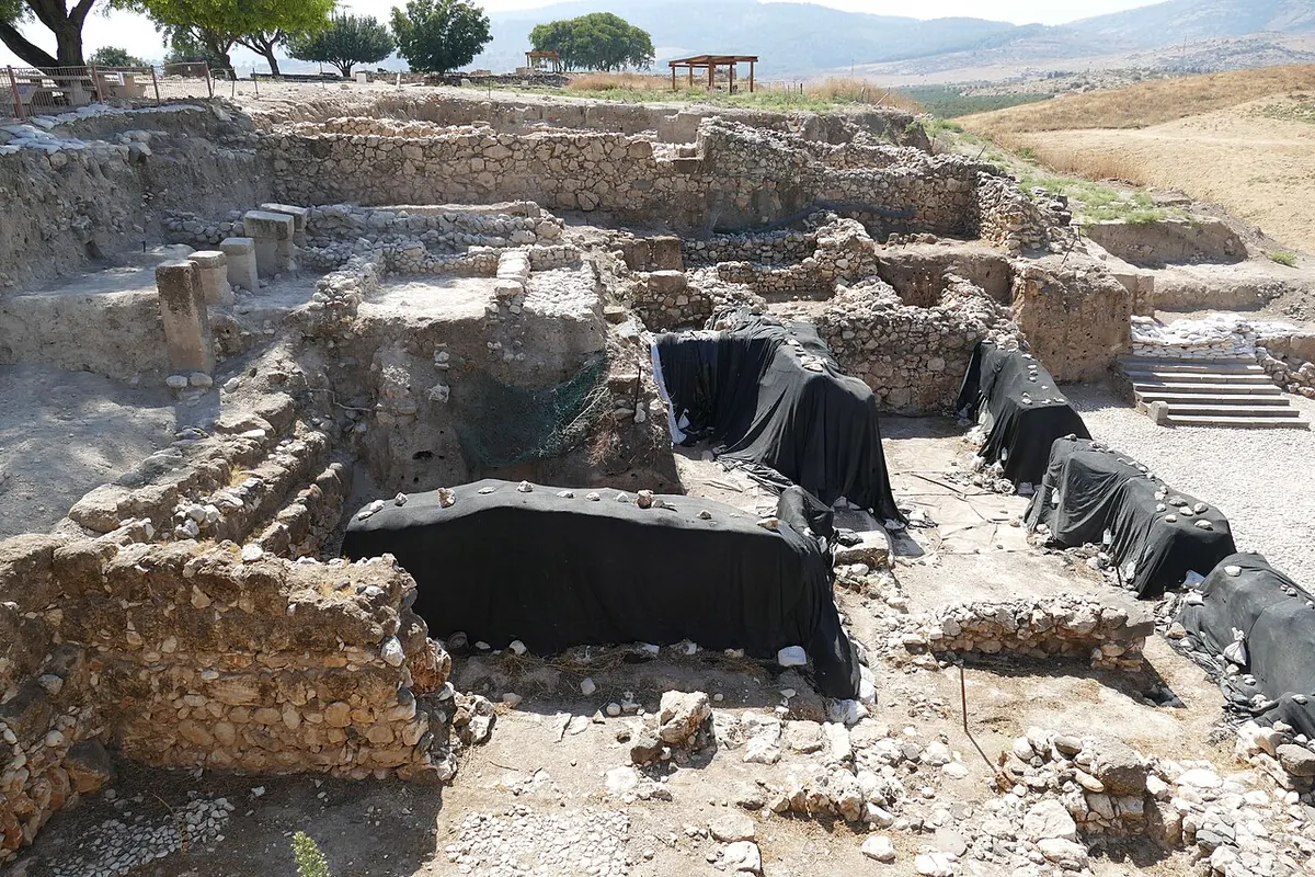 שטח חפירה ארכיאולוגית עם קירות אבן נמוכים, וחלקים מכוסים ביריעות שחורות.
